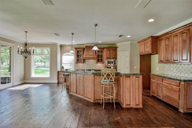 kitchen featuring backsplash, stainless steel microwave, a notable chandelier, dark hardwood / wood-style flooring, and an island with sink