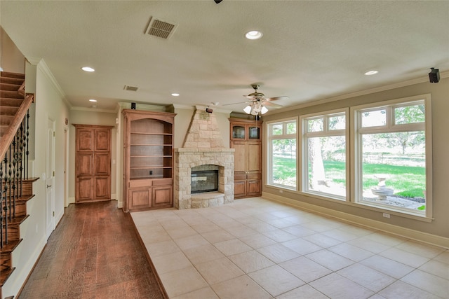 unfurnished living room with a textured ceiling, ceiling fan, crown molding, and a stone fireplace