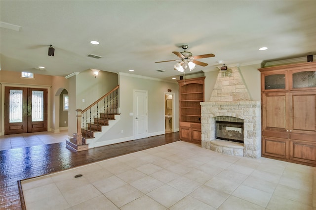 unfurnished living room featuring light hardwood / wood-style flooring, ornamental molding, french doors, ceiling fan, and a stone fireplace