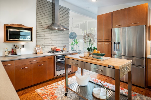 kitchen featuring appliances with stainless steel finishes, lofted ceiling, light hardwood / wood-style flooring, and wall chimney range hood