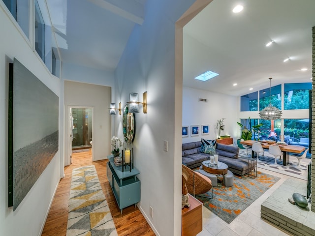 living room featuring high vaulted ceiling, light wood-type flooring, and a skylight