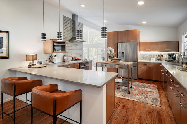 kitchen with sink, wall chimney exhaust hood, kitchen peninsula, built in appliances, and a breakfast bar