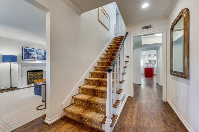 stairway featuring a premium fireplace, hardwood / wood-style flooring, and crown molding