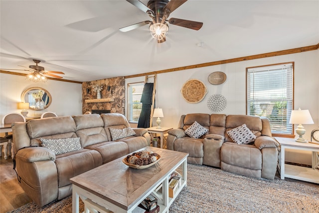 living room featuring ceiling fan, crown molding, hardwood / wood-style floors, and a stone fireplace