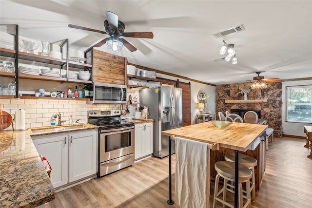 kitchen with appliances with stainless steel finishes, light hardwood / wood-style flooring, white cabinetry, and a stone fireplace