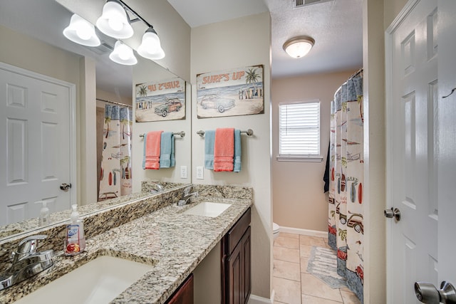 bathroom featuring toilet, double vanity, tile patterned floors, and a textured ceiling