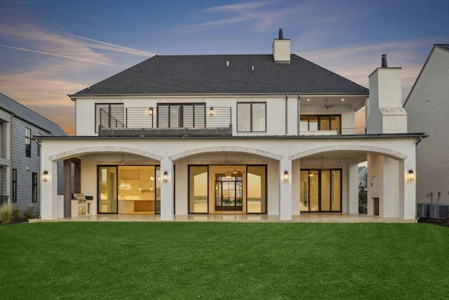 back house at dusk with a yard, a patio area, ceiling fan, and a balcony