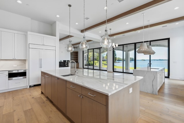 kitchen featuring a water view, white cabinetry, sink, and a large island with sink