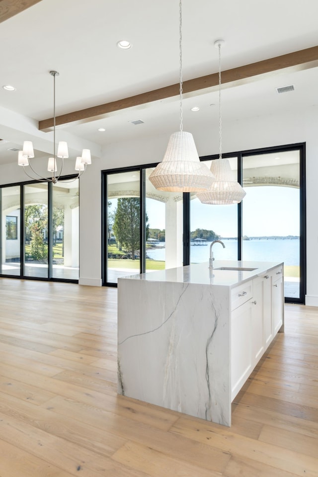 kitchen featuring sink, light hardwood / wood-style flooring, pendant lighting, a water view, and white cabinets