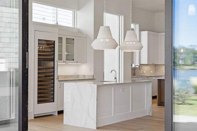 kitchen with white cabinets, light wood-type flooring, an island with sink, and beverage cooler