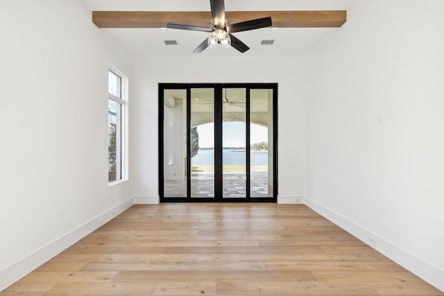 empty room featuring ceiling fan, light hardwood / wood-style flooring, a water view, and beamed ceiling