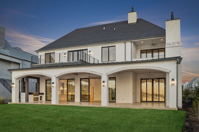 back house at dusk with a yard, ceiling fan, a balcony, and a patio