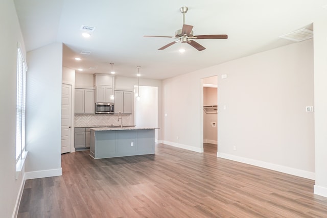 kitchen with gray cabinets, hardwood / wood-style floors, decorative backsplash, a kitchen island with sink, and ceiling fan