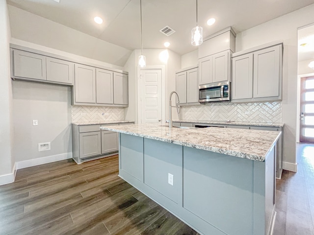 kitchen with decorative light fixtures, tasteful backsplash, dark hardwood / wood-style flooring, a kitchen island with sink, and light stone countertops