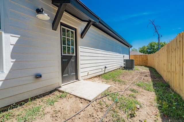 view of exterior entry featuring central AC unit and fence