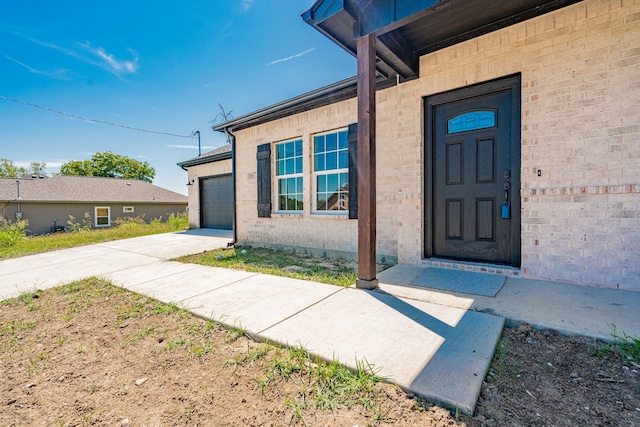 entrance to property with brick siding, an attached garage, and concrete driveway