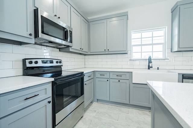 kitchen featuring light stone counters, tasteful backsplash, gray cabinetry, sink, and appliances with stainless steel finishes