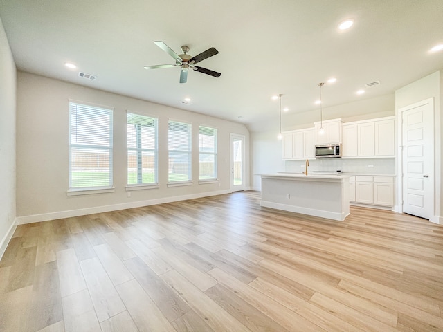 unfurnished living room featuring a wealth of natural light, sink, ceiling fan, and light hardwood / wood-style flooring