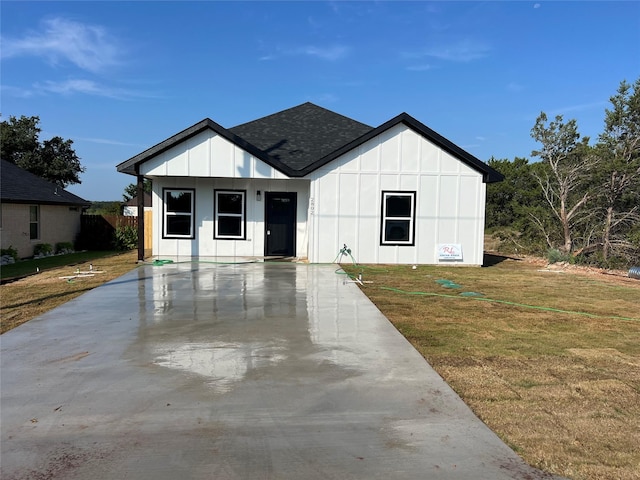 modern farmhouse featuring a shingled roof, a front lawn, and board and batten siding