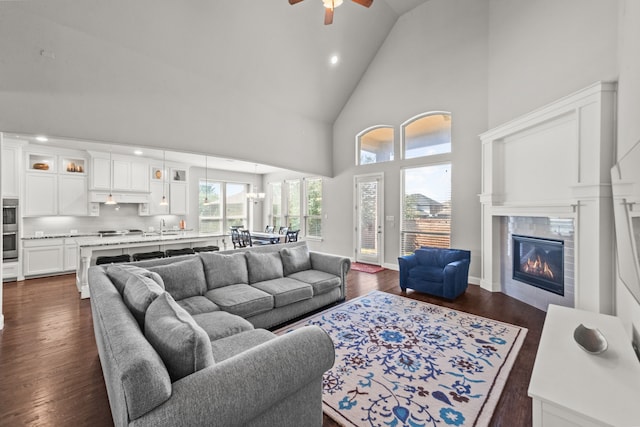 living room featuring ceiling fan, dark wood-type flooring, high vaulted ceiling, a tiled fireplace, and sink