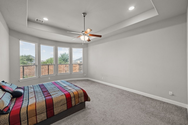 carpeted bedroom featuring a tray ceiling and ceiling fan