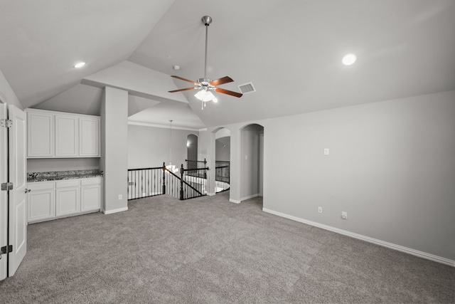 unfurnished living room with vaulted ceiling, ceiling fan with notable chandelier, and light carpet