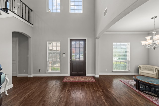 entrance foyer featuring hardwood / wood-style flooring, a towering ceiling, a notable chandelier, and ornamental molding