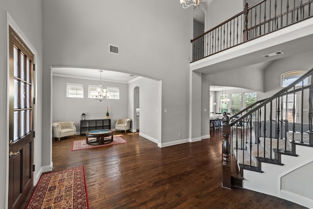 foyer with a towering ceiling, wood-type flooring, a notable chandelier, and crown molding