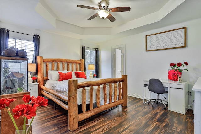 bedroom with ceiling fan, dark wood-type flooring, and a tray ceiling