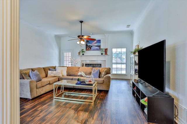 living room with ceiling fan, hardwood / wood-style flooring, a tiled fireplace, and crown molding