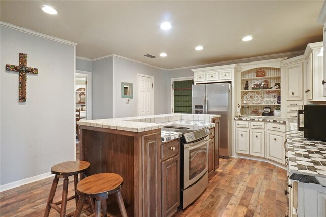 kitchen with appliances with stainless steel finishes, ornamental molding, wood-type flooring, a kitchen island, and a breakfast bar