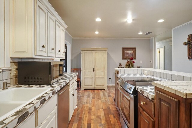 kitchen with light hardwood / wood-style flooring, electric range oven, tile counters, stainless steel dishwasher, and crown molding