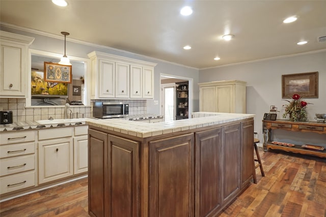 kitchen with dark wood-type flooring, pendant lighting, ornamental molding, and tasteful backsplash