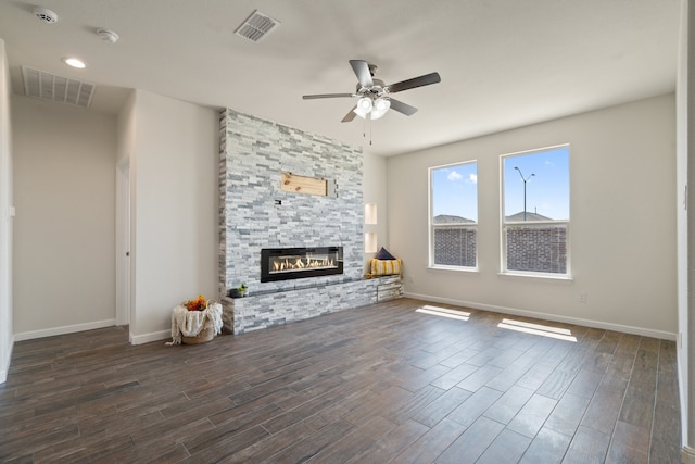 unfurnished living room featuring a stone fireplace, dark hardwood / wood-style floors, and ceiling fan