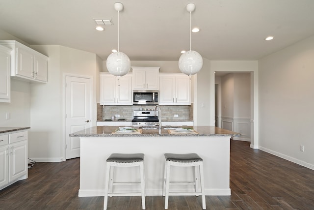 kitchen with white cabinetry, appliances with stainless steel finishes, an island with sink, and dark hardwood / wood-style floors