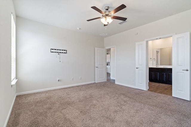 unfurnished bedroom featuring ensuite bath, dark colored carpet, and ceiling fan