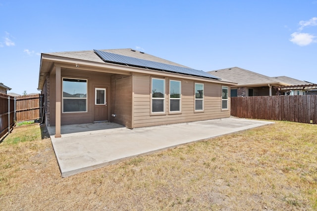 rear view of property featuring solar panels, a patio, and a lawn