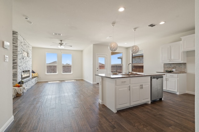 kitchen with a stone fireplace, white cabinetry, dishwasher, and plenty of natural light