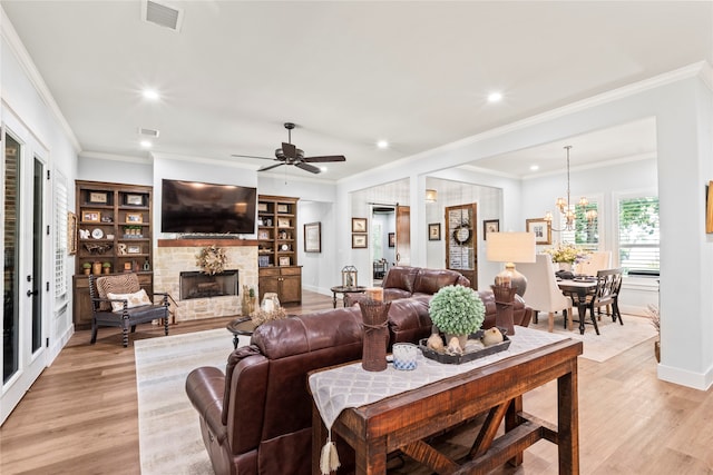 living room featuring light hardwood / wood-style flooring, ornamental molding, built in shelves, ceiling fan, and a stone fireplace