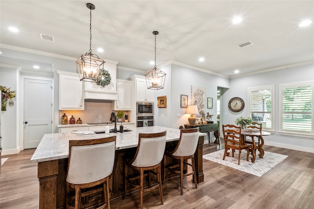 kitchen featuring decorative backsplash, wood-type flooring, white cabinets, a breakfast bar, and a center island with sink