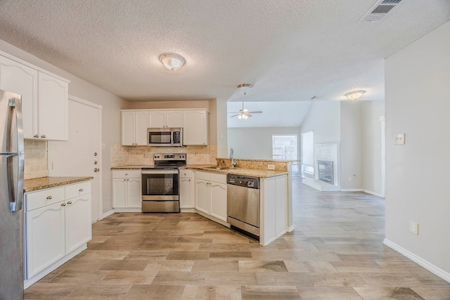 kitchen featuring appliances with stainless steel finishes, light stone counters, white cabinets, kitchen peninsula, and a textured ceiling