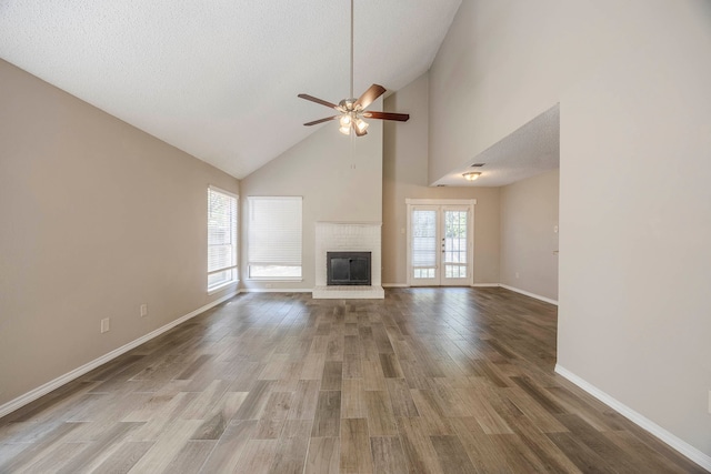 unfurnished living room featuring wood-type flooring, a textured ceiling, a fireplace, high vaulted ceiling, and ceiling fan