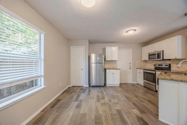 kitchen featuring white cabinets, sink, light hardwood / wood-style flooring, stainless steel appliances, and dark stone countertops