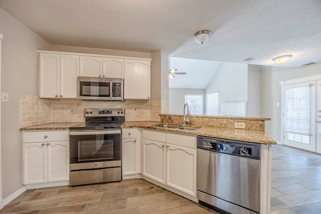 kitchen featuring sink, white cabinets, lofted ceiling, kitchen peninsula, and appliances with stainless steel finishes