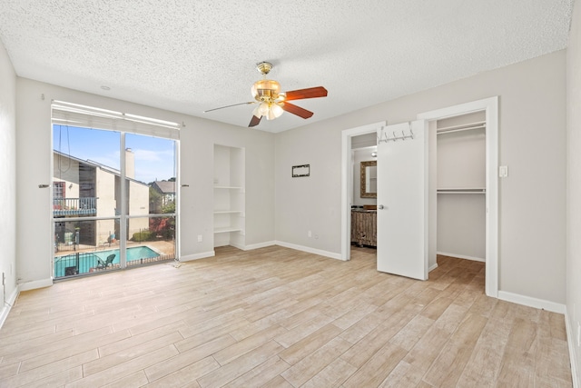 unfurnished bedroom featuring ceiling fan, a spacious closet, a textured ceiling, and light hardwood / wood-style flooring