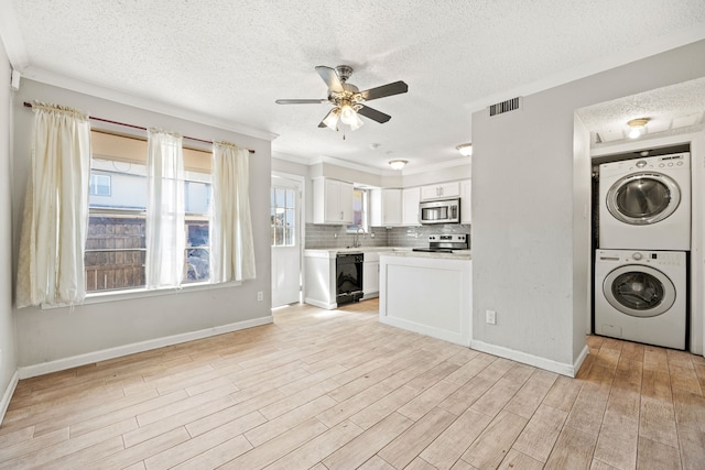 washroom featuring stacked washer / drying machine, light hardwood / wood-style flooring, ceiling fan, and a textured ceiling