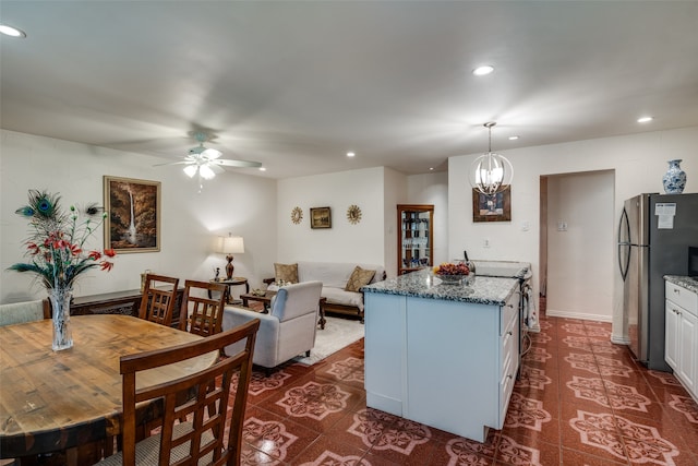 kitchen with a center island, decorative light fixtures, ceiling fan with notable chandelier, stainless steel refrigerator, and white cabinets