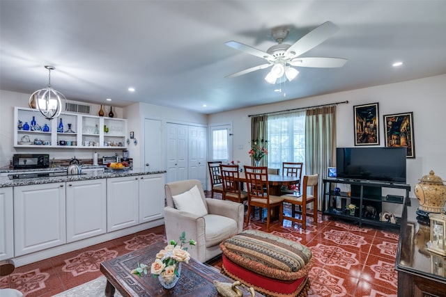 tiled living room with ceiling fan with notable chandelier