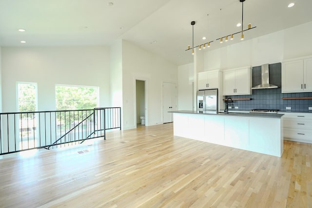 kitchen featuring stainless steel appliances, pendant lighting, white cabinetry, and wall chimney range hood