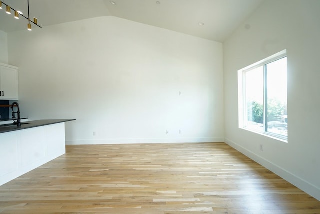 unfurnished living room featuring light wood-type flooring, vaulted ceiling, and sink